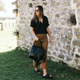 Woman holding a black leather tote
handbag against a stone wall