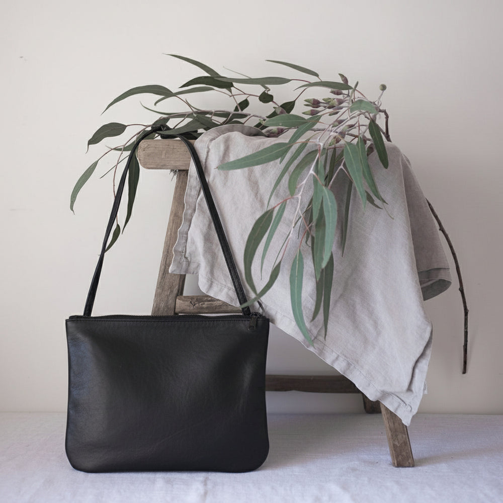 Black handbag on a white surface with a wooden stool and greenery in the background