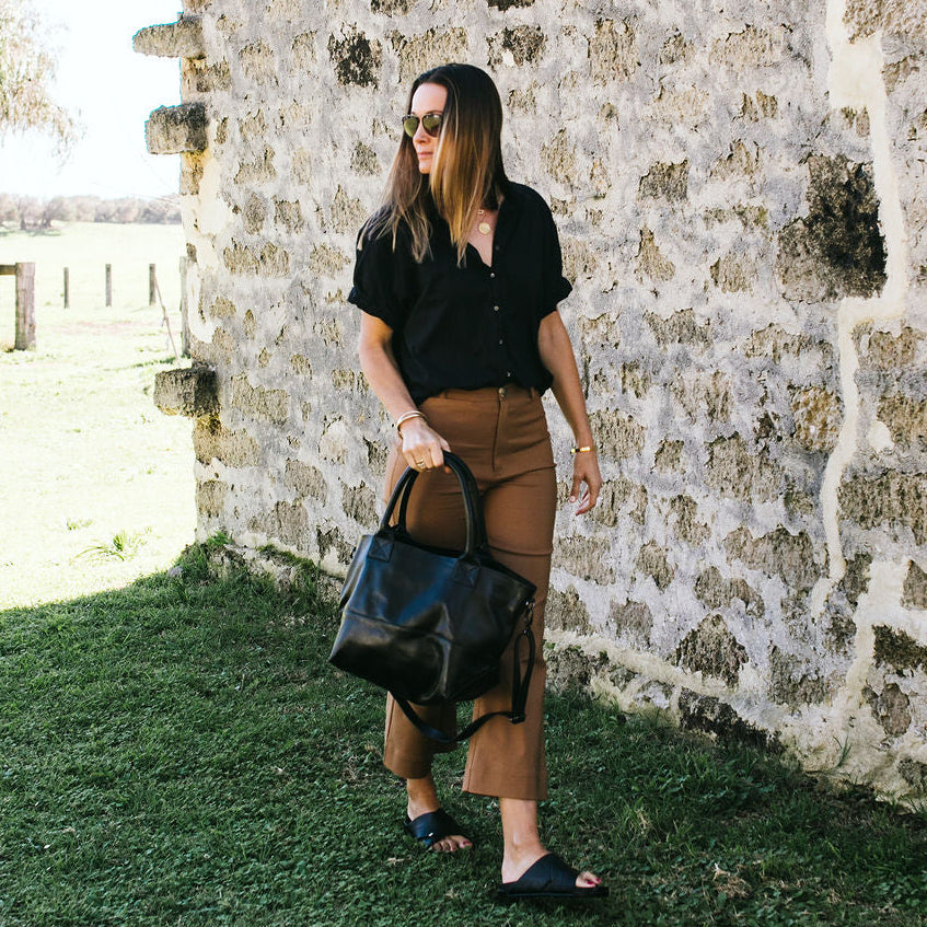 Woman holding a black leather tote 
handbag against a stone wall