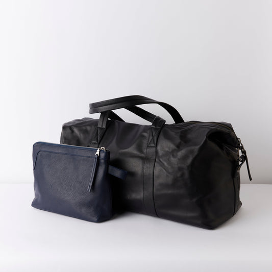 Black leather weekender / duffel bag and Navy toiletry bag on a white background