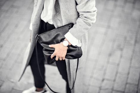 Woman in black jeans with grey coat holding a black bag with strap haging down